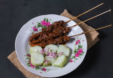 Endonezya spesiyalitesi tavuk satay ve dilimlenmiş çiğ soğan serpiştirilmiş seramik tabakta. Siyah bir arkaplanda izole edilmiş