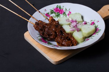 Endonezya spesiyalitesi tavuk satay ve dilimlenmiş çiğ soğan serpiştirilmiş seramik tabakta. Siyah bir arkaplanda izole edilmiş
