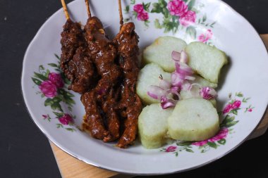 Endonezya spesiyalitesi tavuk satay ve dilimlenmiş çiğ soğan serpiştirilmiş seramik tabakta. Siyah bir arkaplanda izole edilmiş