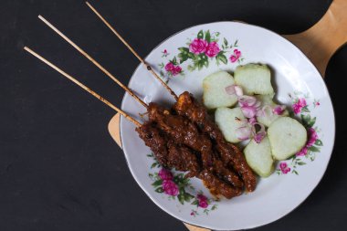 Endonezya spesiyalitesi tavuk satay ve dilimlenmiş çiğ soğan serpiştirilmiş seramik tabakta. Siyah bir arkaplanda izole edilmiş