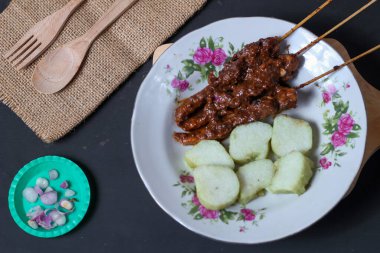 Endonezya spesiyalitesi tavuk satay ve dilimlenmiş çiğ soğan serpiştirilmiş seramik tabakta. Siyah bir arkaplanda izole edilmiş