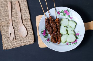 Endonezya spesiyalitesi tavuk satay ve dilimlenmiş çiğ soğan serpiştirilmiş seramik tabakta. Siyah bir arkaplanda izole edilmiş