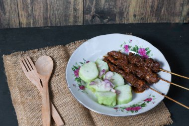 Endonezya spesiyalitesi tavuk satay ve dilimlenmiş çiğ soğan serpiştirilmiş seramik tabakta. Siyah bir arkaplanda izole edilmiş