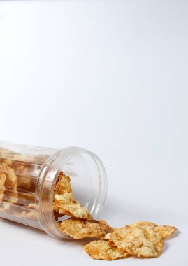 Beyaz arka planda izole edilmiş plastik bir kavanozun içinden sızan melinjo krakerleri.