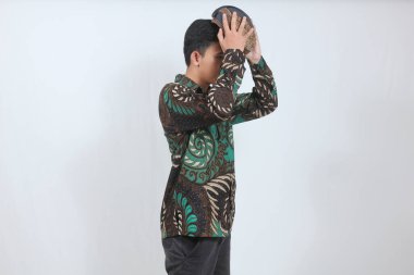 Soyut batik gömlek giyen Asyalı adam beyaz arka planda izole edilmiş Blangkon şapkasını çıkarıyor.