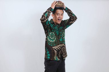 Batik gömlek giyen Asyalı bir adam portresi ve beyaz arka planda izole edilmiş Cava Blangkon şapkası.