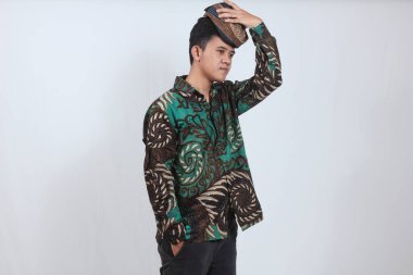 Soyut batik gömlek giyen Asyalı adam beyaz arka planda izole edilmiş Blangkon şapkasını çıkarıyor.