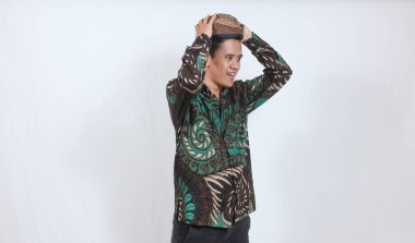 Batik gömlek giyen Asyalı bir adam portresi ve beyaz arka planda izole edilmiş Cava Blangkon şapkası.