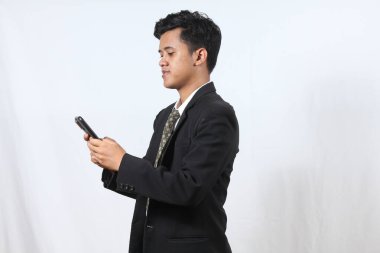 Siyah takım elbiseli Asyalı bir ofis çalışanı elinde akıllı telefon tutarak müşteriye pazarlık mesajı gönderiyor, beyaz arka planda izole edilmiş. İş ve teknoloji kavramı.