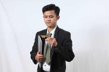 Siyah takım elbiseli Asyalı bir adam dizüstü bilgisayar ve özel kredi kartını beyaz arka planda tutuyor.