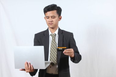 Siyah takım elbiseli Asyalı bir adam dizüstü bilgisayar ve özel kredi kartını beyaz arka planda tutuyor.