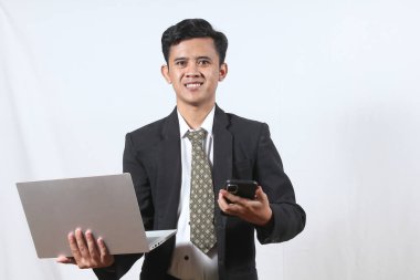 Asyalı işadamı cep telefonu ve dizüstü bilgisayarlı neşeli ifade yüklü bir maaşla proje üzerinde çalışıyor.