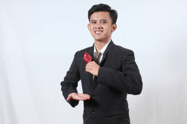 Asyalı işadamı gülümseyerek beyaz arka planda izole edilmiş kredi kartını tutuyor.