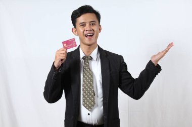 Asyalı işadamı gülümseyerek beyaz arka planda izole edilmiş kredi kartını tutuyor.