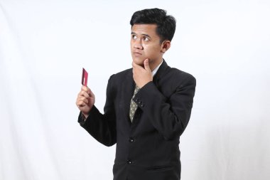 Siyah takım elbiseli Asyalı işadamı kredi kartını beyaz arka planda tutarken şaşkın hissediyor