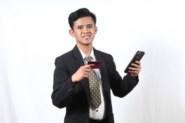 Genç Asyalı iş adamının portresi beyaz arka planda izole edilmiş akıllı telefondan kredi kartıyla online alışveriş yapmaktan çok mutlu.