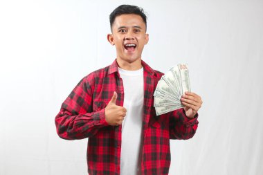 Asyalı adam kırmızı ekose gömlek giyip çok para kazanırken başparmak kaldırırken neşeli görünüyor.