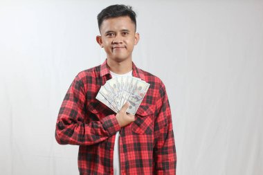 Kırmızı kareli gömlek giyen Asyalı bir adam beyaz arka planda izole edilmiş bir sürü 100 dolarlık banknot tutuyor.