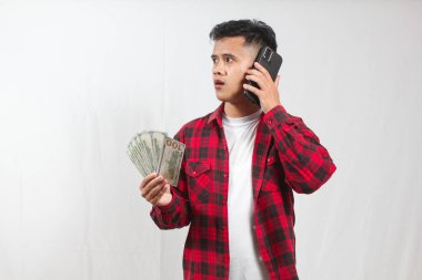 Asyalı bir adam ciddi bir ifadeyle bir sürü dolar tutarken bir telefon görüşmesi yapıyor.