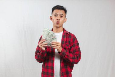 Kırmızı kareli gömlek giyen Asyalı bir adam beyaz arka planda izole edilmiş bir sürü 100 dolarlık banknot tutuyor.