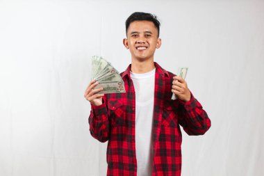 Kırmızı kareli gömlek giyen Asyalı bir adam beyaz arka planda izole edilmiş bir sürü 100 dolarlık banknot tutuyor.