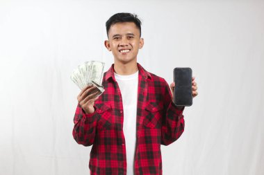 Asyalı adamın elinde dolar banknotu var ve gülümseyen bir ifadeyle boş cep telefonu gösteriyor. İş ve teknoloji kavramı.