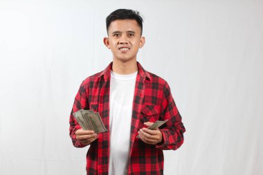 Kareli gömlek giyen Asyalı bir adam bir sürü yüz dolarlık banknot tutuyor.