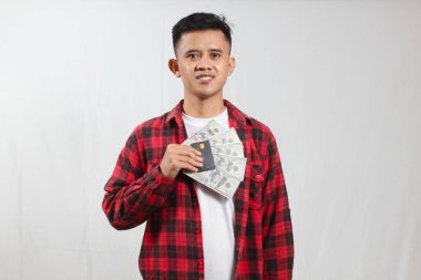 Ekose gömlek giyen Asyalı bir adam yığınla para ve kredi kartı gösteriyor.