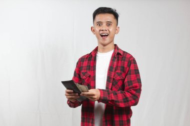 Kareli gömlek giyen Asyalı adam beyaz arka planda izole edilmiş cüzdandan dolar alıyor.