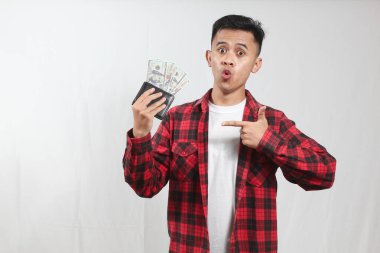 Asyalı bir adam, içinde bir sürü dolar olan, şaşırmış bir ifadeyle dolu kalın bir cüzdanı işaret eder.