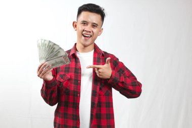 Kareli gömlek giyen Asyalı bir adam beyaz arka planda izole edilmiş 100 dolarlık banknotu işaret ediyor.