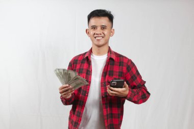 Ekose gömlek giyen Asyalı bir adam dolar banknotları taşıyor ve akıllı telefonlar çekiyor. İyi haberler alıyor, piyango kazanıyor.