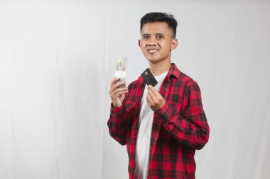 Kareli tişört giyen Asyalı bir adam yüksek kaliteli siyah kredi kartı ve dolar banknotu tutuyor.