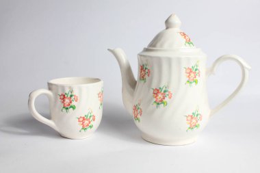 Beyaz arka planda izole edilmiş çiçek desenli beyaz seramik çaydanlık ve fincan