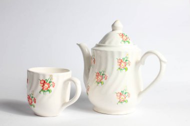 Beyaz arka planda izole edilmiş çiçek desenli beyaz seramik çaydanlık ve fincan