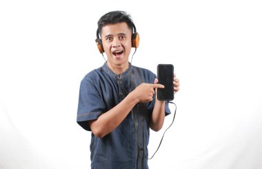 Kot pantolon giyen Asyalı adam elinde cep telefonu, müzik listesi seçiyor ve kulaklıkla müzik dinliyor.