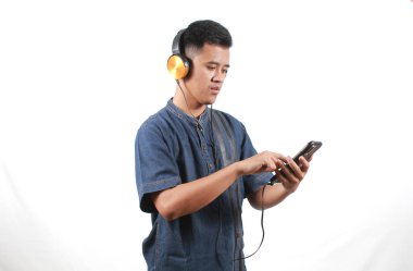 Kot pantolon giyen Asyalı adam elinde cep telefonu, müzik listesi seçiyor ve kulaklıkla müzik dinliyor.