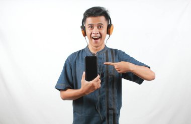 Kot gömlek giyen Asyalı adam müzik dinliyor ve akıllı telefonu işaret ediyor.