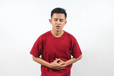 Kırmızı tişört giyen Asyalı bir adam beyaz arka planda karnı ağrıyor.