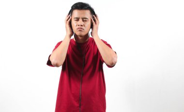 Kırmızı tişört giyen Asyalı adam kulaklıklardan müzik dinlerken gözleri kapalı beyaz arka planda.