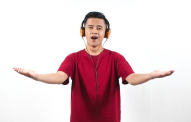 Kırmızı tişört giyen Asyalı adam kulaklıklardan müzik dinlerken gözleri kapalı beyaz arka planda.