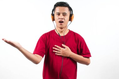 Kırmızı tişörtlü Asyalı adam kulaklıklardan müzik dinliyor ve yarışma için ses eğitimi alıyor.