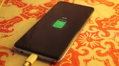 Akıllı telefon şarjı, sarı spot ışıkları olan batik desenli masa örtüsünde% 87 güç gösteriyor.