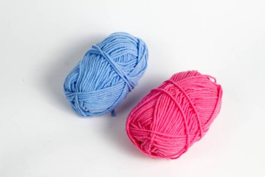 Pembe ve mavi yün iplik, beyaz bir arkaplanda izole edilmiş oval bir şekle sokulmuş.
