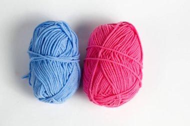 Pembe ve mavi yün iplik, beyaz bir arkaplanda izole edilmiş oval bir şekle sokulmuş.