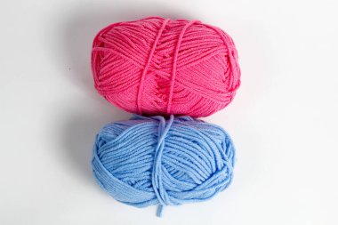 Pembe ve mavi yün iplik, beyaz bir arkaplanda izole edilmiş oval bir şekle sokulmuş.