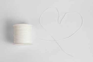 Beyaz naylon iplik plastik bir kılıfa düzgünce sarılmış, sicim beyaz bir arka planda izole edilmiş bir kalp şekli oluşturuyor.
