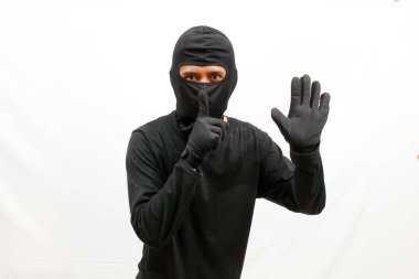 Siyah elbiseli hırsız, beyaz arka planda izole edilmiş bir şekilde işaret vermek için parmaklarını dudaklarına koyar.