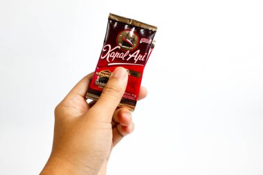 Indonesia, Sukoharjo - June 19, 2025 : holding a sachet of ground coffee product  steamer (Kapal Api )brand from Indonesia, Isolated on white background
