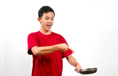 Asyalı bir adam elinde kızartma tavası tutarken şaşırmış bir ifadeyle yiyeceği işaret ediyor.